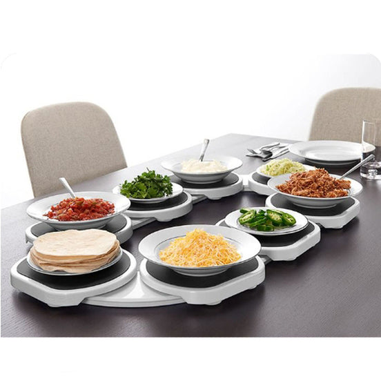 Bandeja giratoria y extensible para servir comida dispuesta a lo largo de una mesa de comedor de madera.