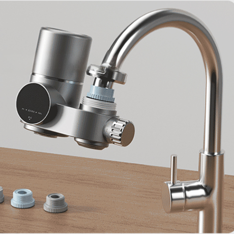 Purificador de agua para grifo en acabado plateado mate con indicador digital y perilla de cambio, instalado en un grifo monomando de cocina con adaptadores de instalación al lado.